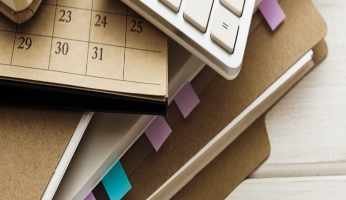 Photo of files, calculator and calendar showing the year end stacked in a pile. 